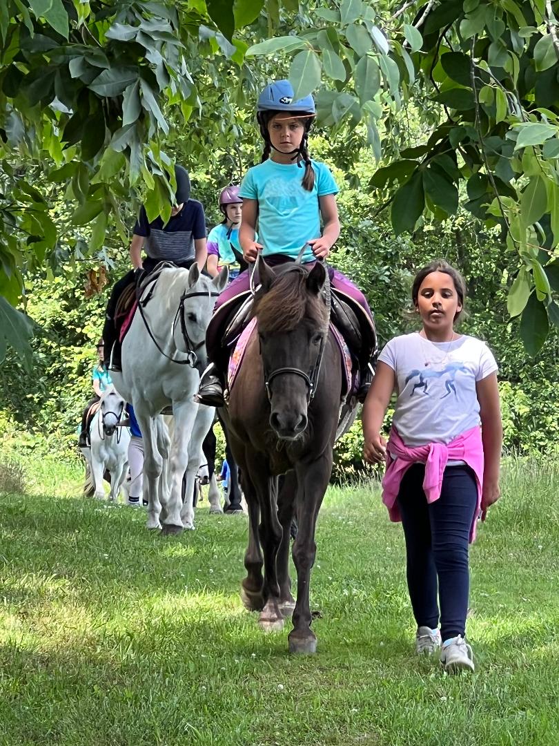 Two girls riding horses on a trail in the woods.