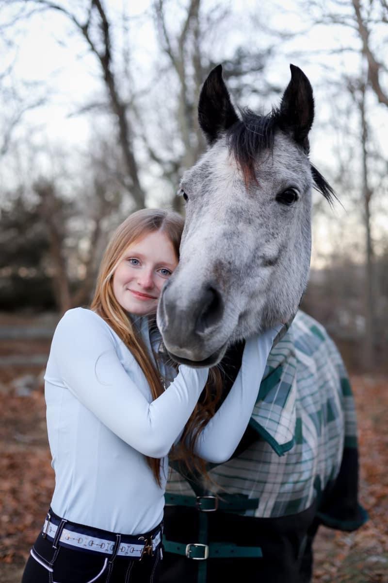 A girl is hugging her horse in the woods.