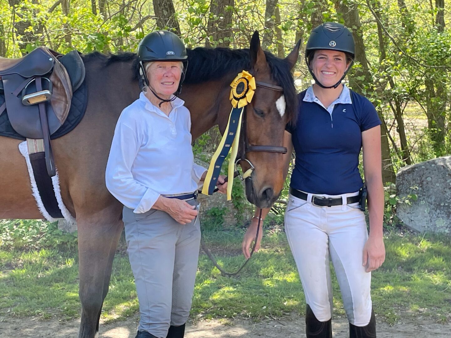 Two women standing next to a horse with a ribbon around its neck.